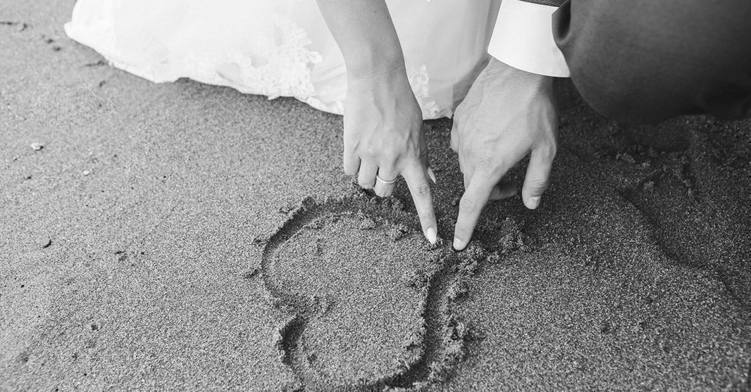砂に指でハートを描くカップルの手元