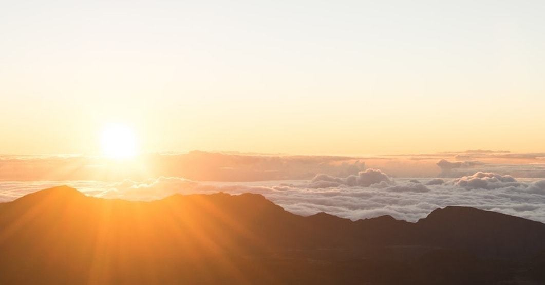 雲海から昇る太陽の手前に浮かぶ山のシルエット