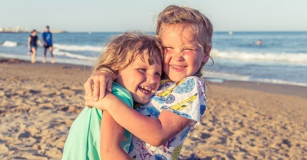 海を背景に笑顔で抱き合う金髪の子供二人