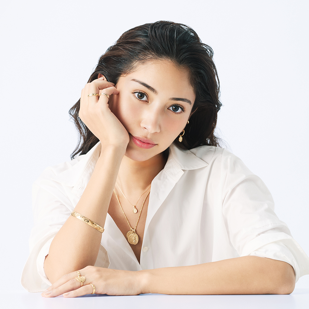 白いシャツを着た黒髪の女性がゴールドのハワイアンジュエリーを着けている