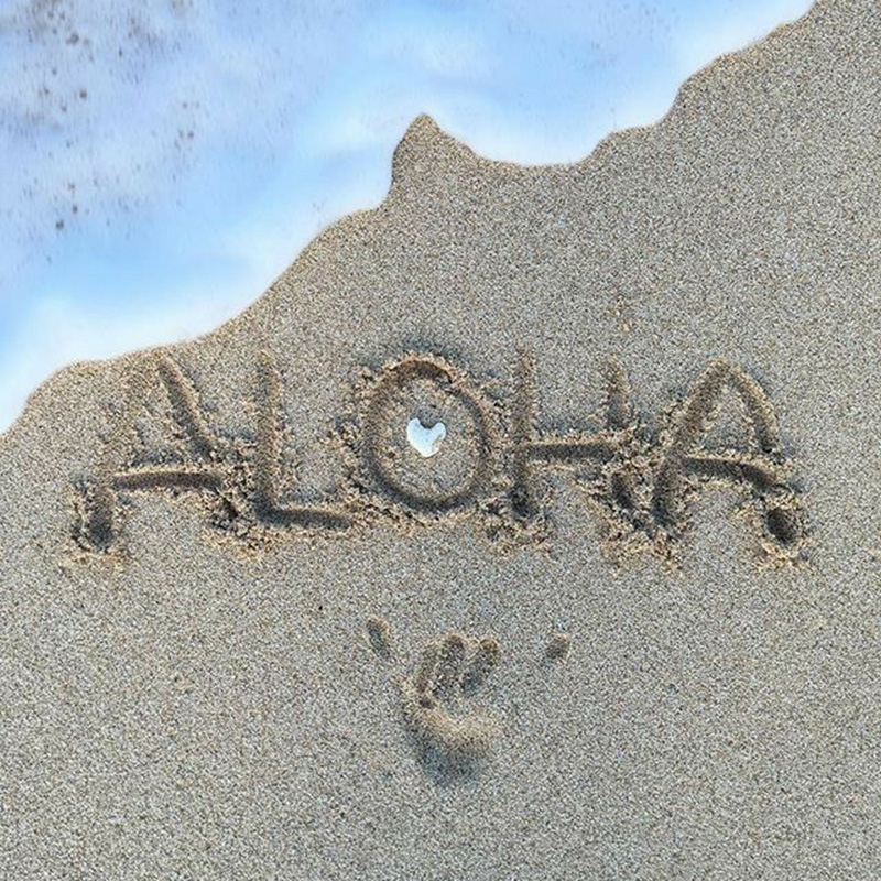 波打ち際にALOHAと砂浜に書かれた文字と貝殻とハンドサイン