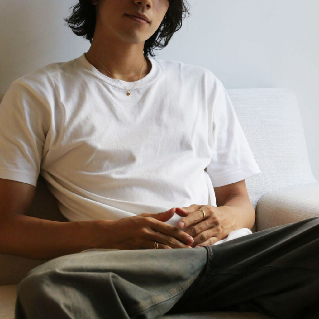 (10001548)ハワイアンジュエリーのネックレスを着用した男性がソファーに座っている